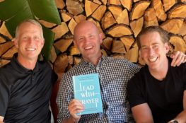 Cameron Doolittle, Peter Greer, and Ryan Skoog pose for a picture holding up their new book Lead with Prayer. Lead with Prayer has a blue cover and white letters.