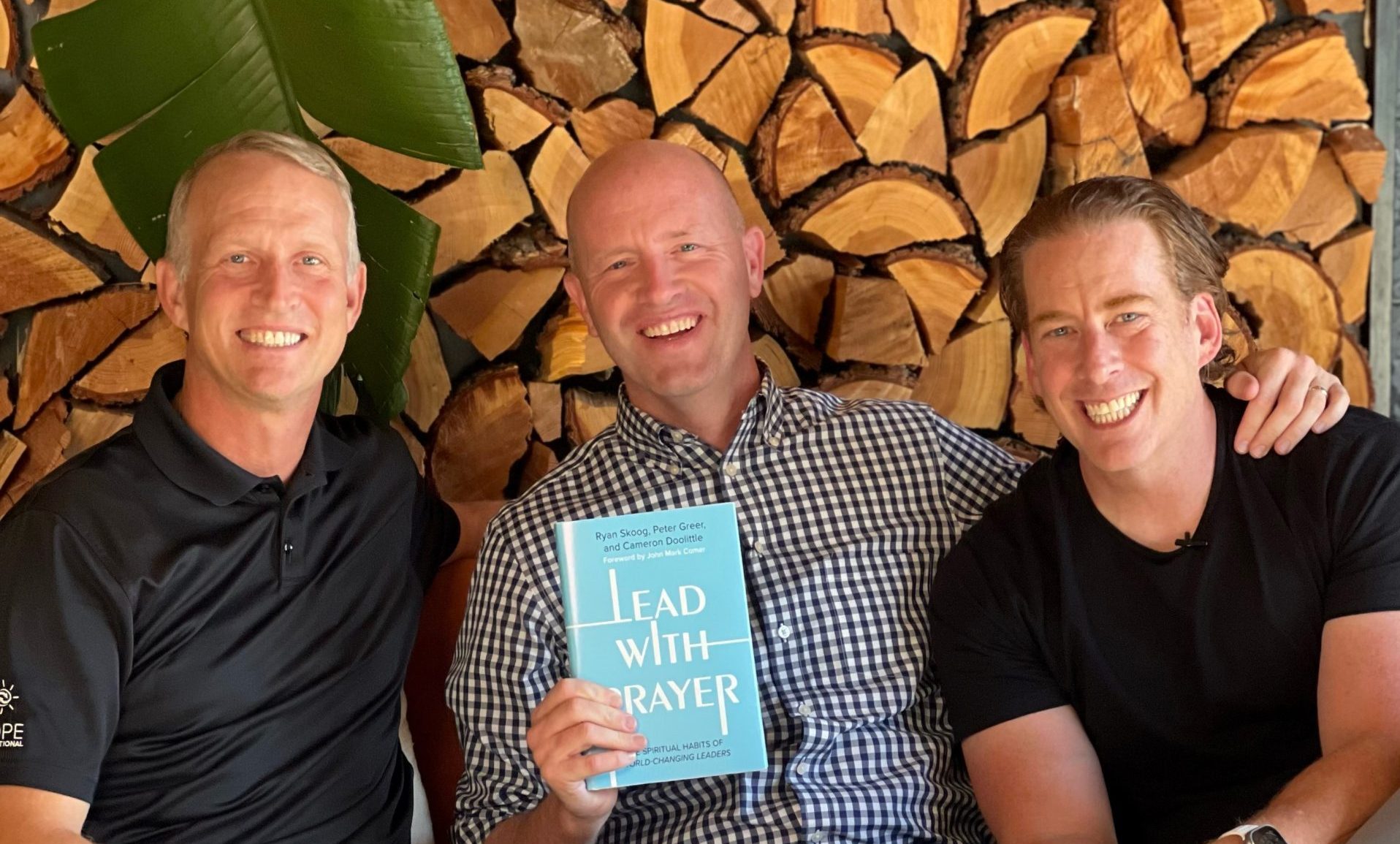 Cameron Doolittle, Peter Greer, and Ryan Skoog pose for a picture holding up their new book Lead with Prayer. Lead with Prayer has a blue cover and white letters.